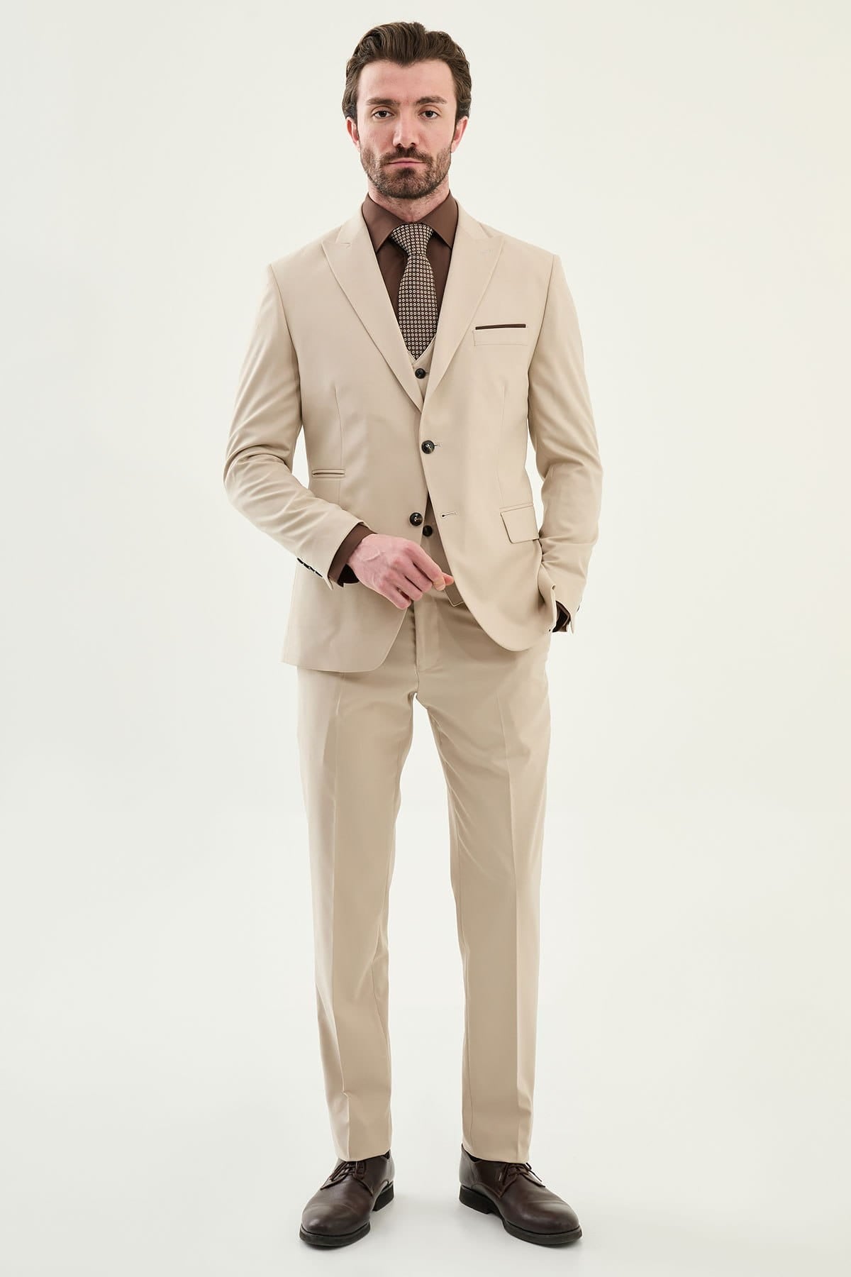 Man wearing a beige suit with a brown shirt and tie on a white background