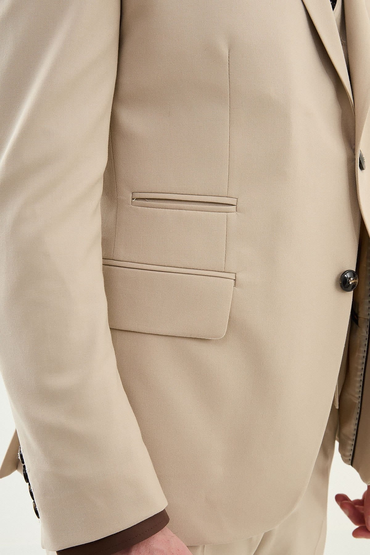 Close-up of a beige suit jacket with a pocket and button detail.