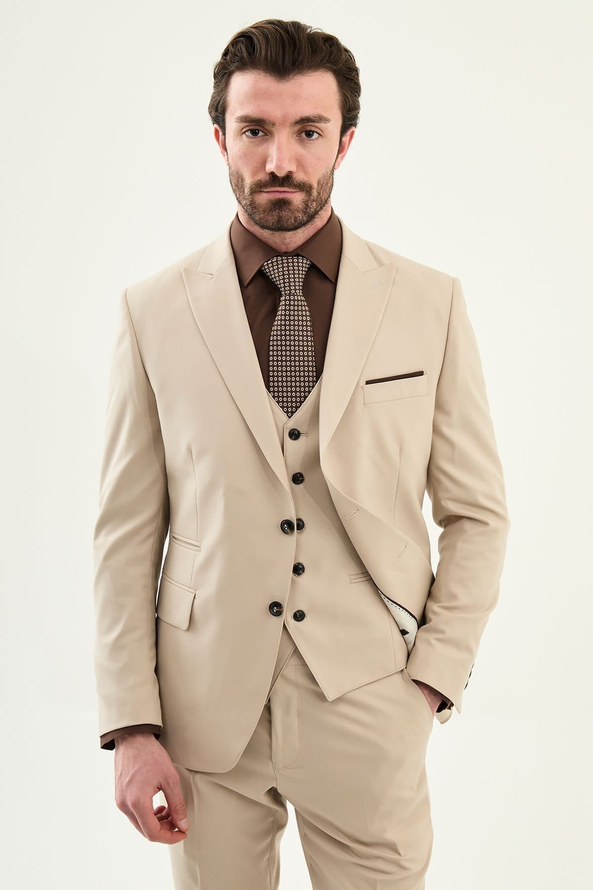 Man wearing a beige suit with a brown shirt and tie on a white background