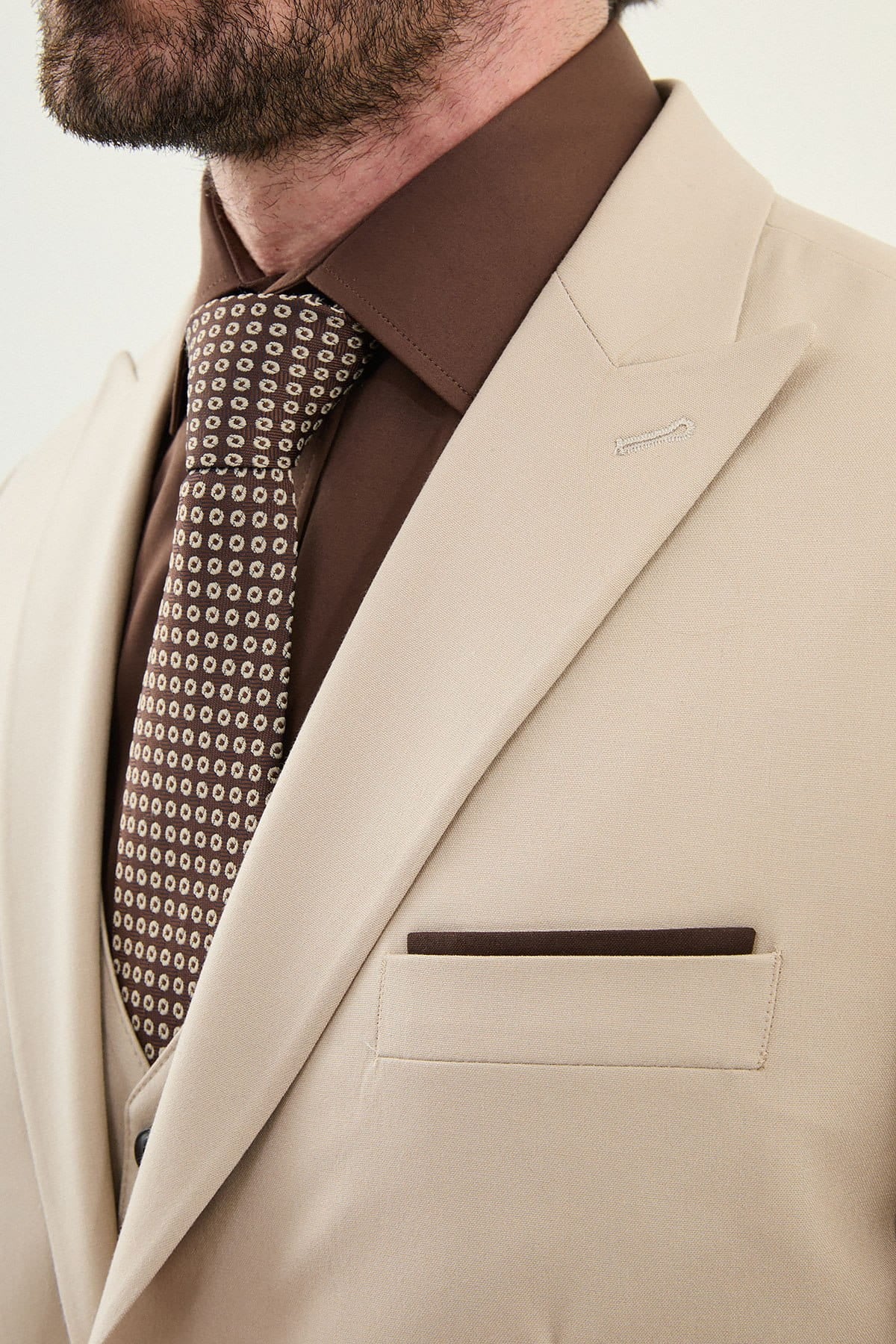 Beige suit jacket with a brown shirt and patterned tie on a neutral background