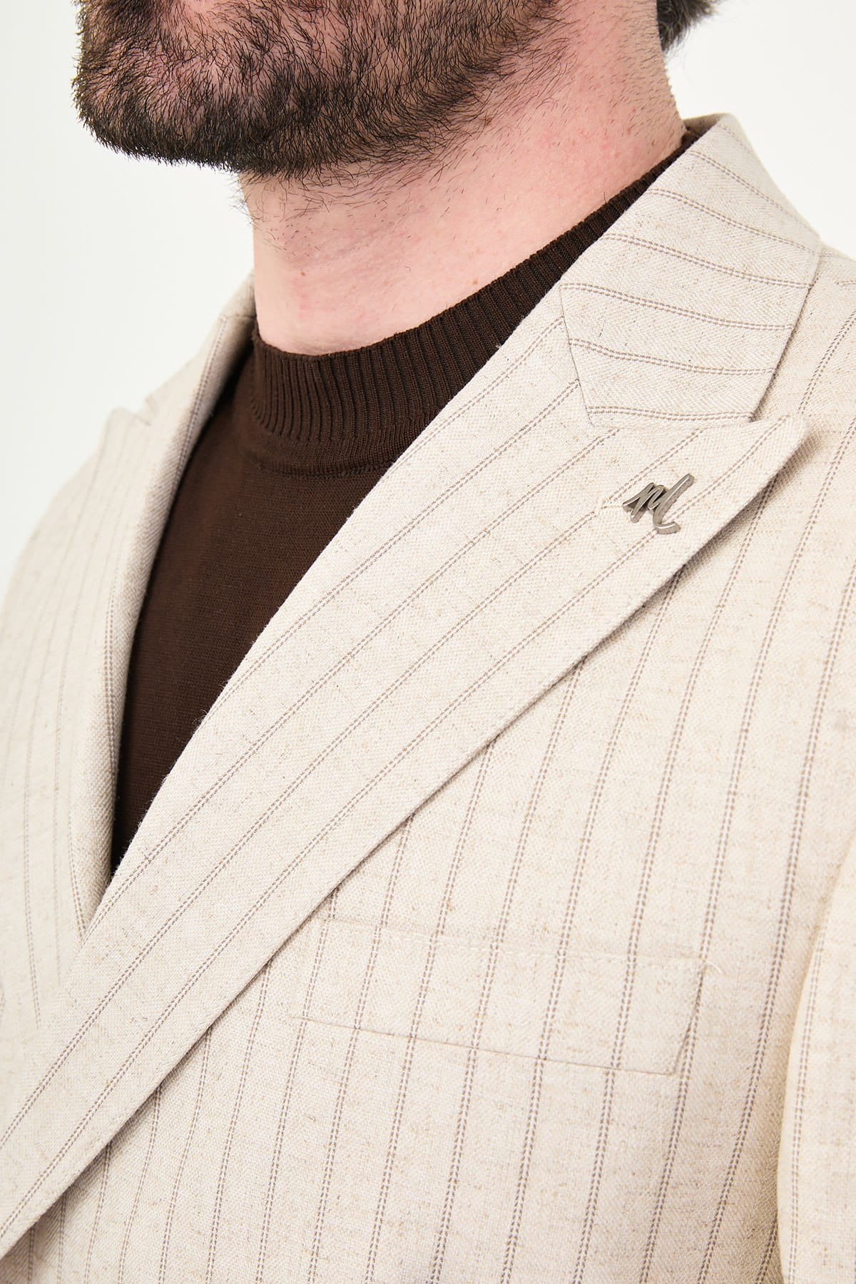 Close-up of a beige pinstripe coat with a brand logo on a neutral background
