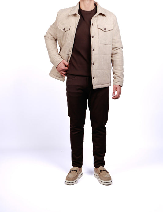 Person wearing a beige quilted jacket, brown shirt, black pants, and beige shoes on a white background