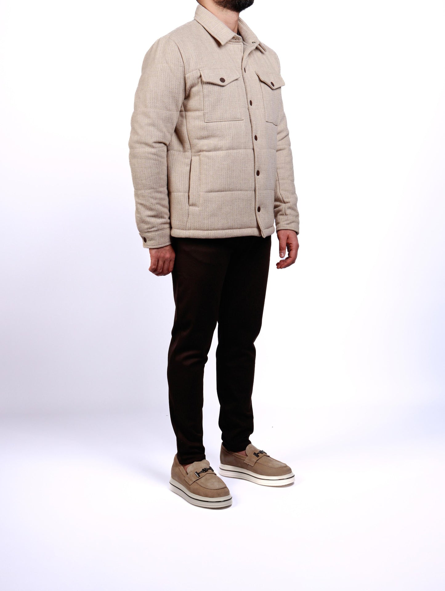Person wearing a beige quilted jacket and black pants on a white background