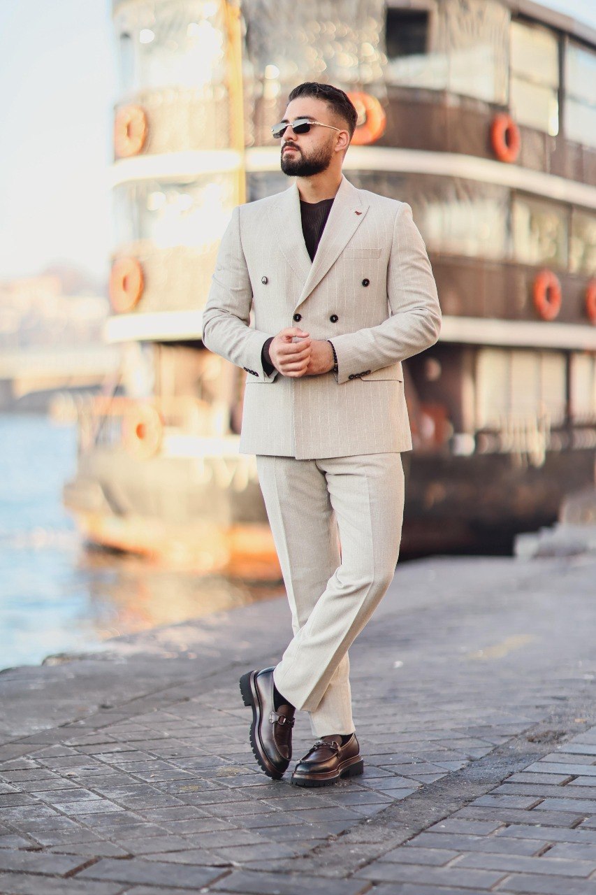 Man in a beige suit walking on a waterfront with a blurred background