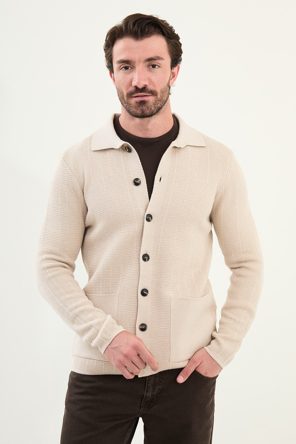 Man wearing a beige button-up cardigan over a dark shirt on a white background