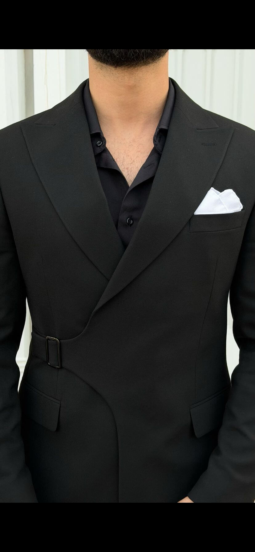 Person wearing a black suit with a white pocket square against a neutral background