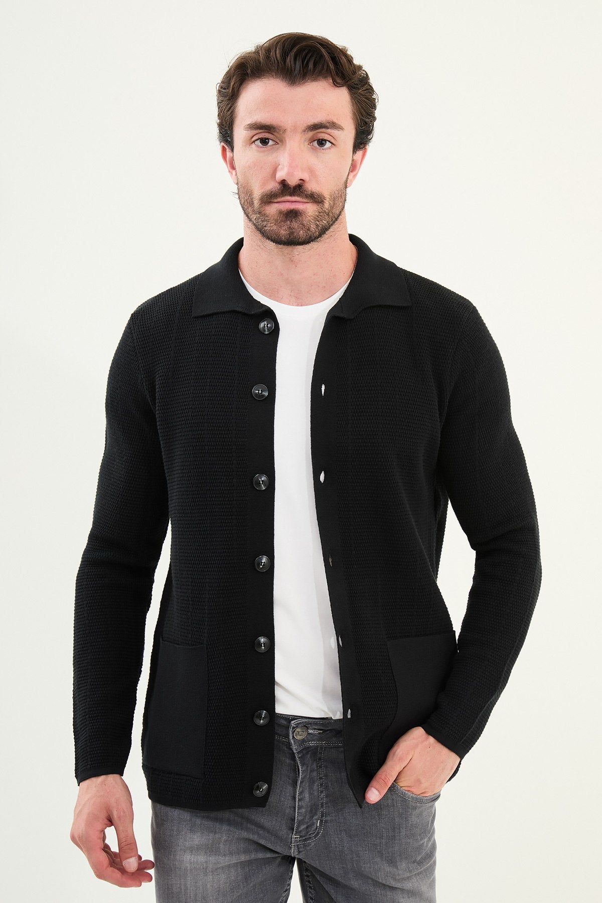 Man wearing a black cardigan over a white shirt on a white background