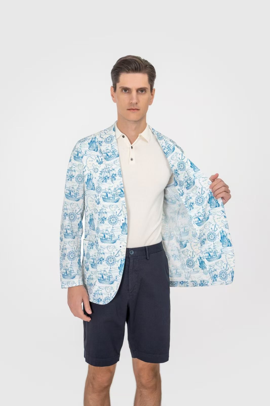 Man wearing a light blue patterned jacket over a white shirt and dark shorts on a white background