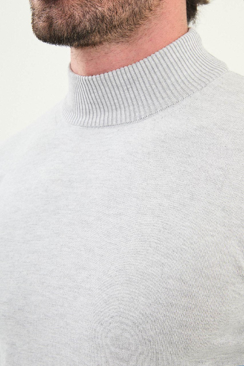 Close-up of a person wearing a light gray sweater with a plain background