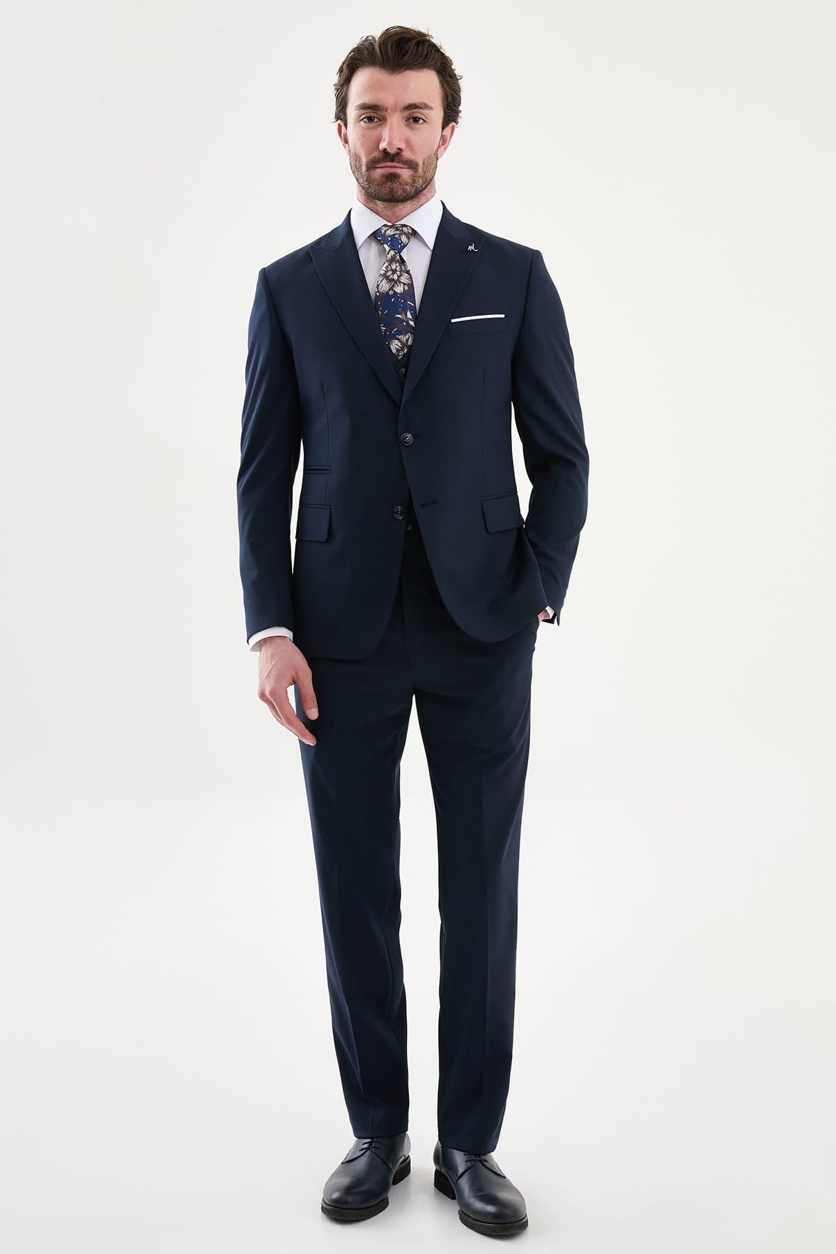 Man wearing a navy suit with a white shirt and patterned tie on a white background