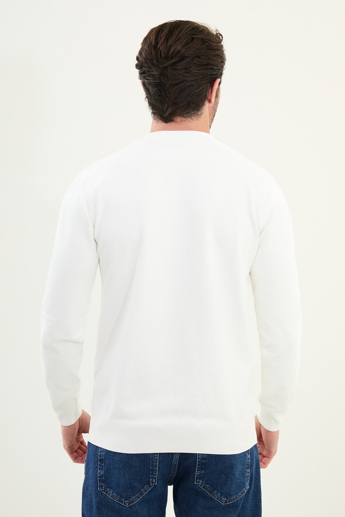 Man wearing a white sweater and blue jeans on a white background