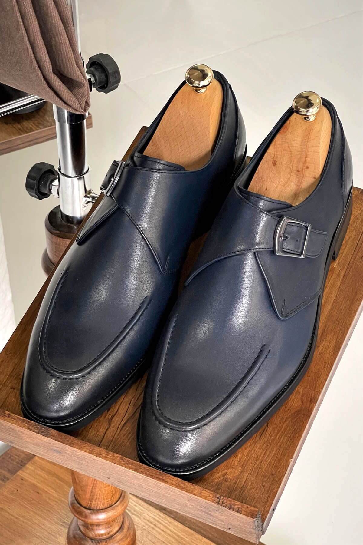 Pair of black leather dress shoes on a wooden stand with a blurred background