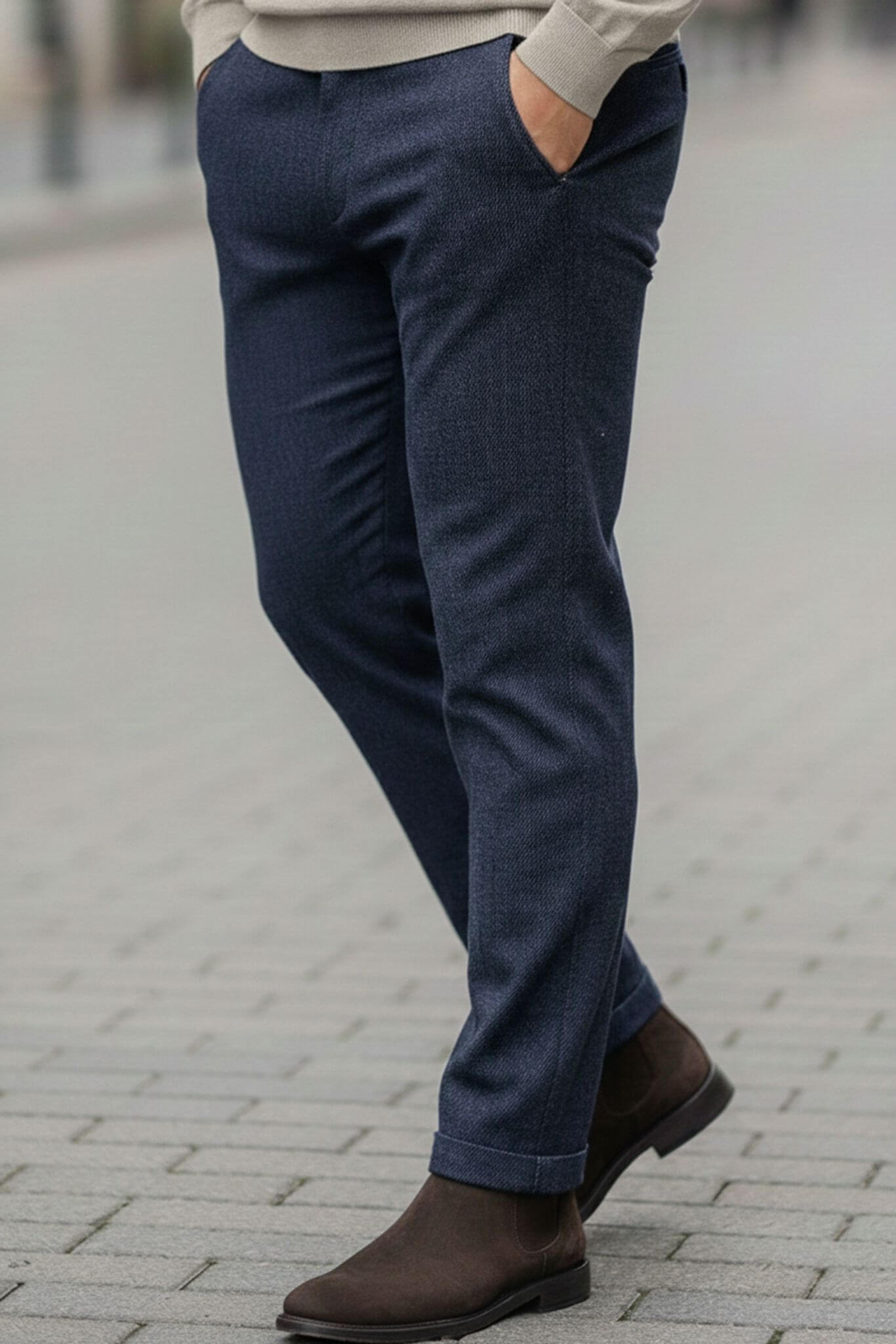 Person wearing navy blue pants and brown shoes on a blurred street background