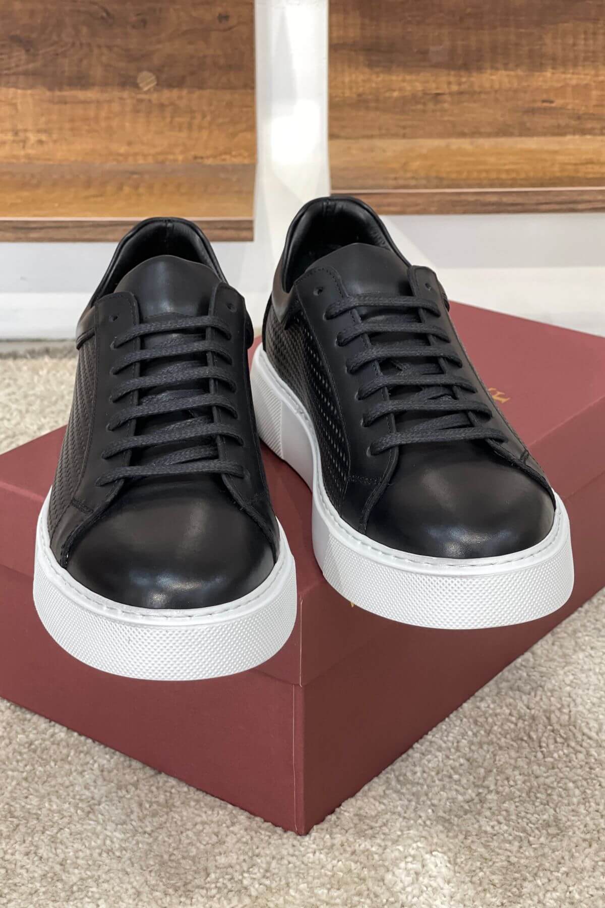 Black sneakers with white soles on a red platform against a wooden background