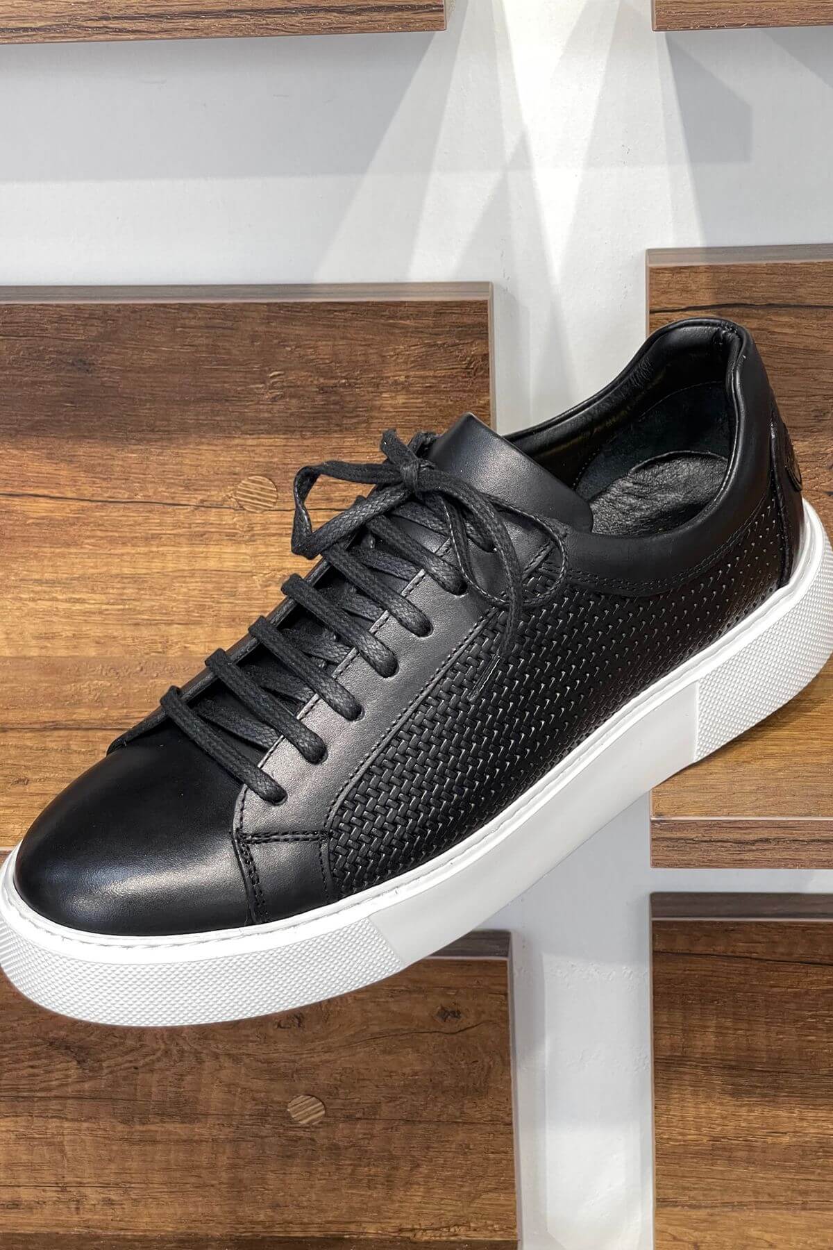 Black sneaker with white sole on a wooden surface