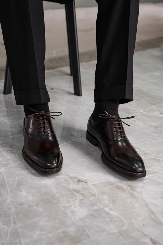 Close-up of men’s regal oxford shoes in rich brown leather with intricate brogue detailing, showcasing luxurious craftsmanship and a timeless design for formal wear.