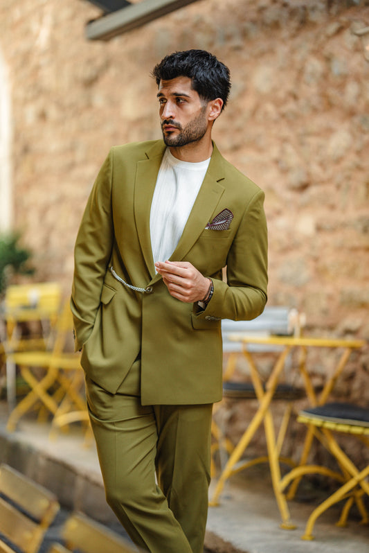 Man in a green suit standing outdoors with tables and chairs in the background
