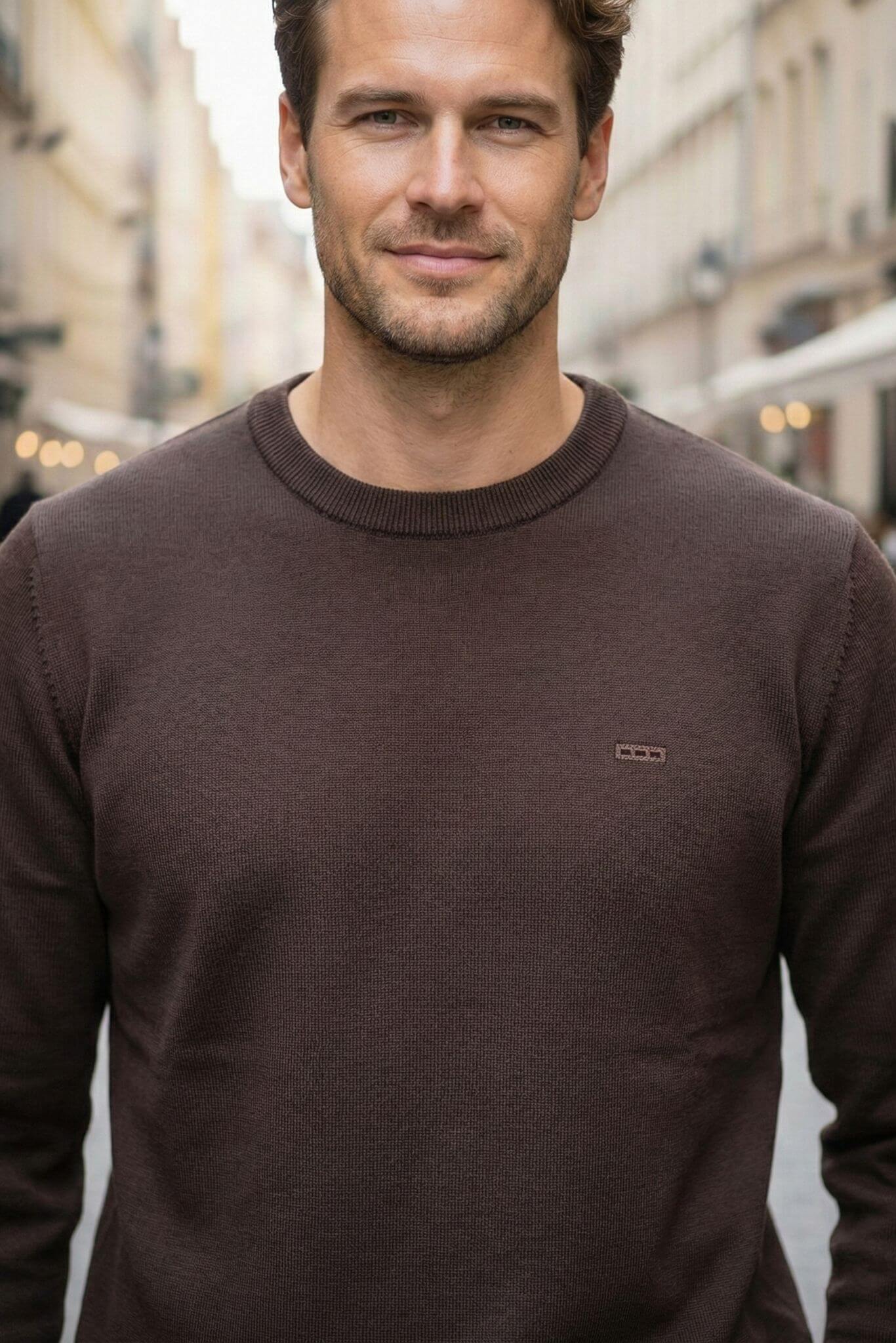 Man wearing a brown sweater standing in an urban setting