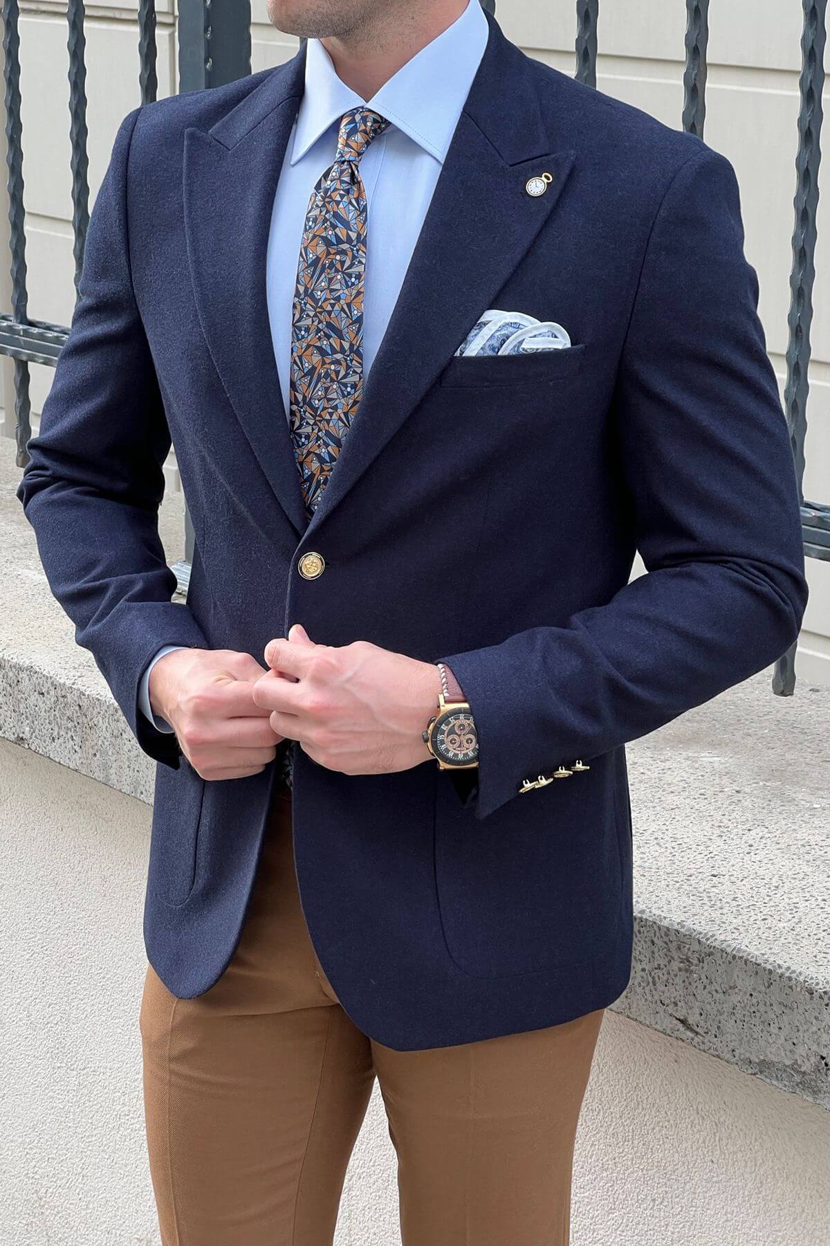 Man wearing a Slim-fit Gold-Buttoned Wool Blend Blazer in Navy Blue, light blue shirt, patterned tie, and brown pants.