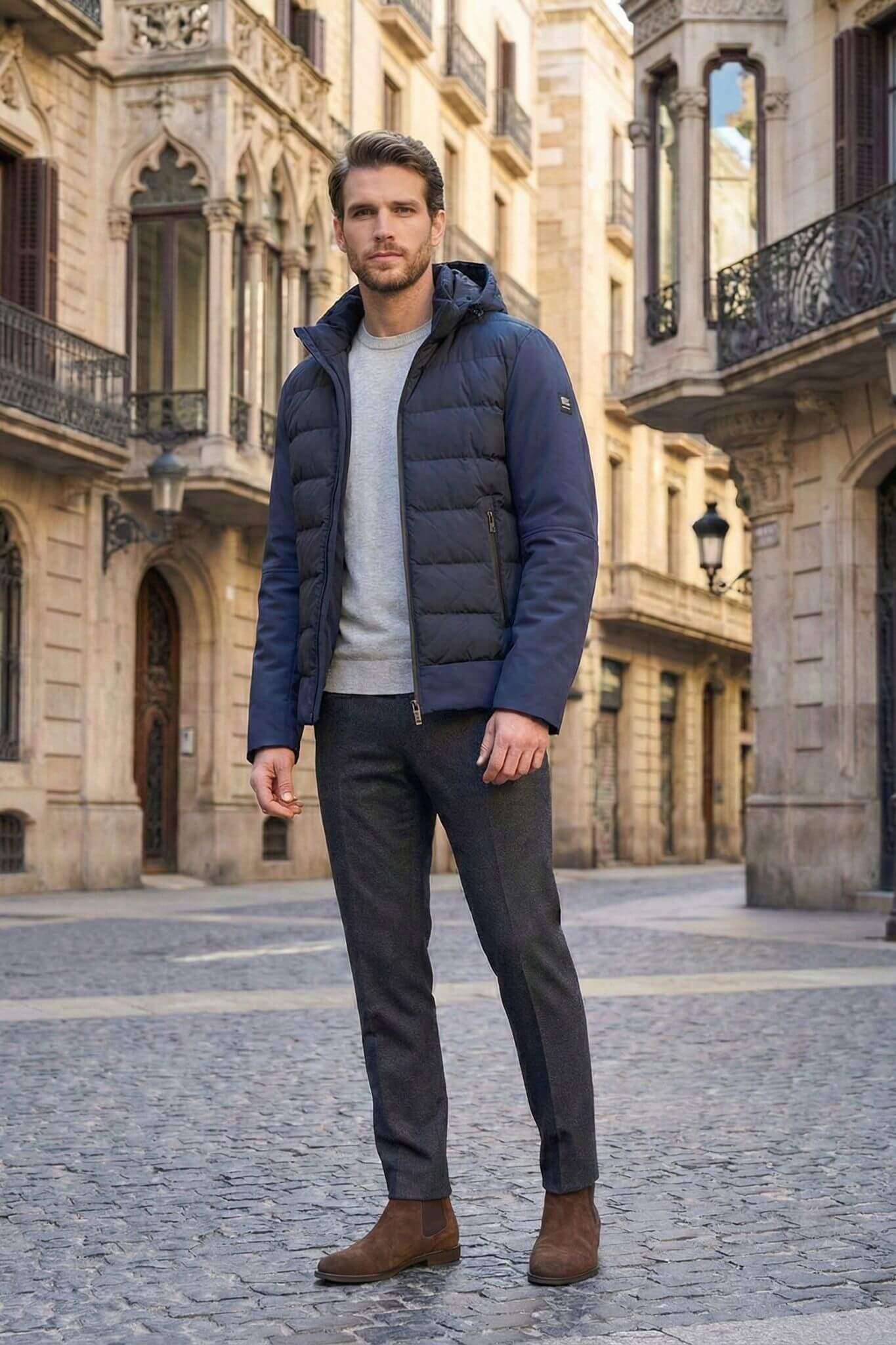 Man wearing a blue puffer jacket standing on a cobblestone street in an urban setting.