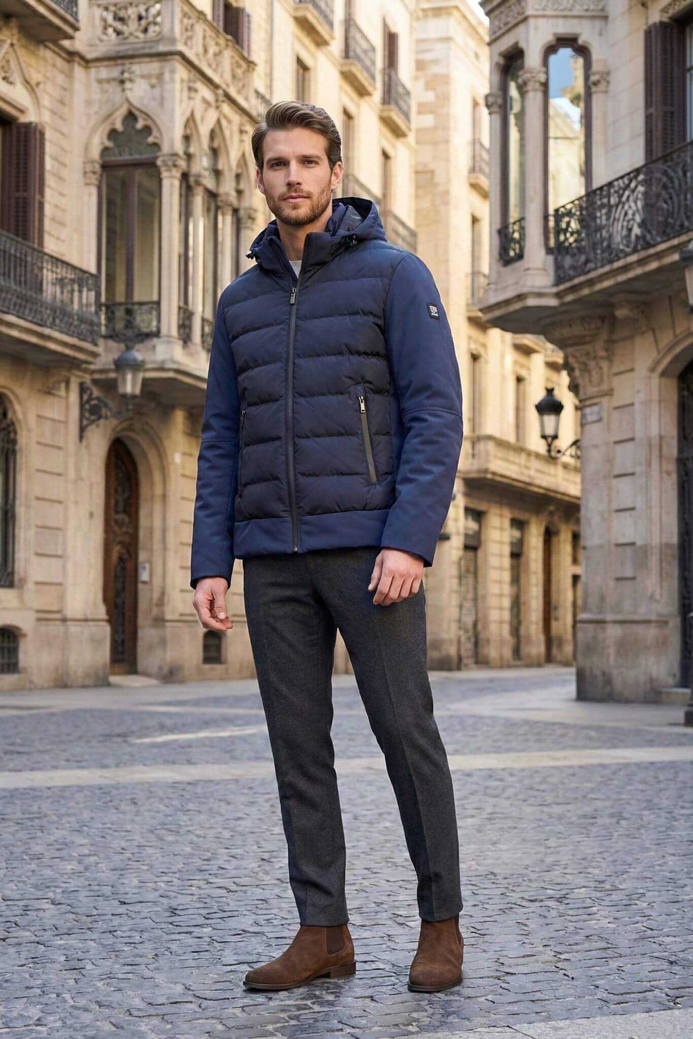 Man wearing a blue puffer jacket standing on a cobblestone street with old buildings.