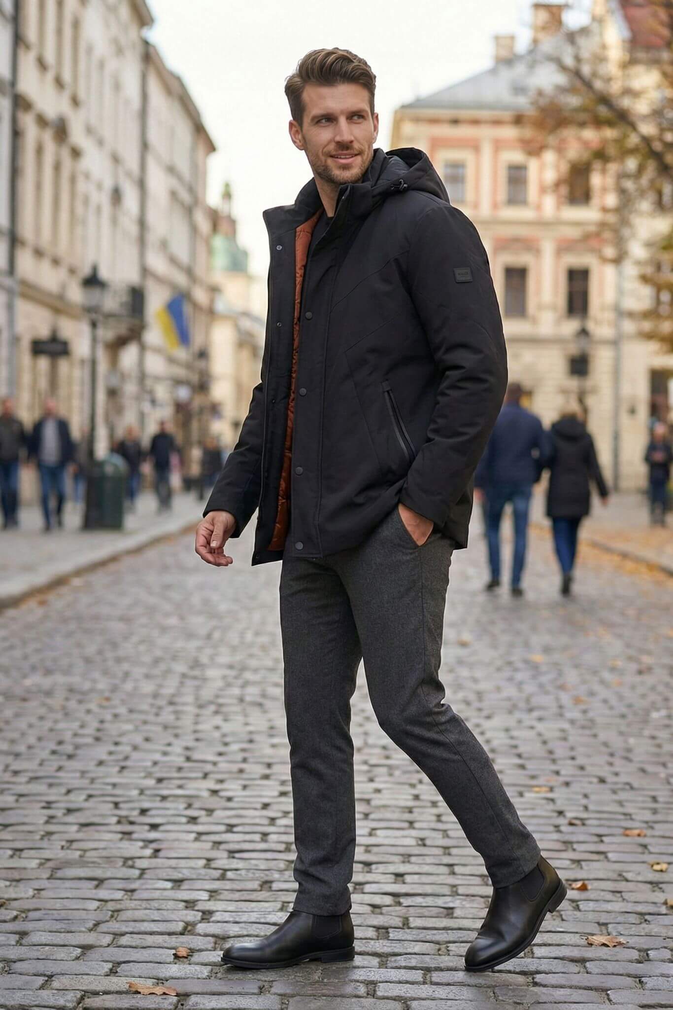 Man wearing a black coat and gray pants walking on a cobblestone street.