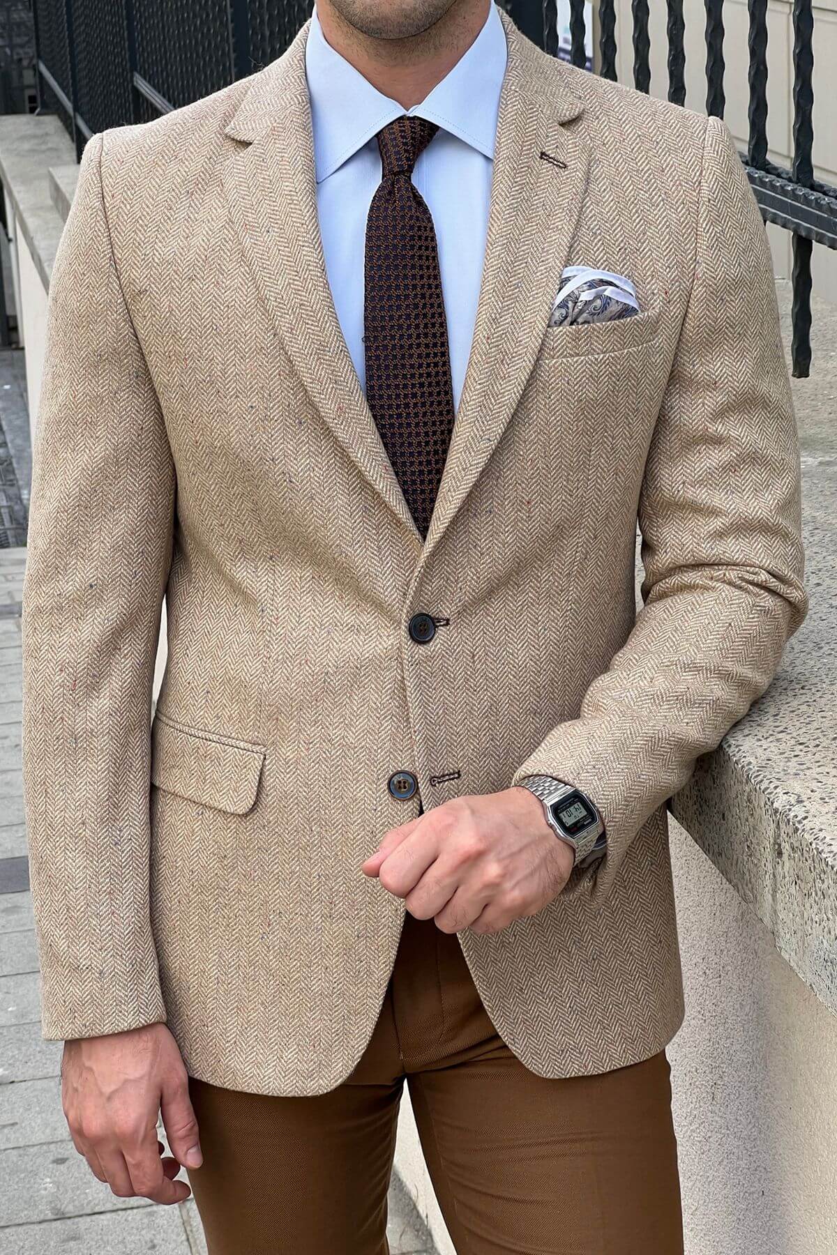 Man wearing a beige blazer, brown pants, and a patterned tie outdoors.