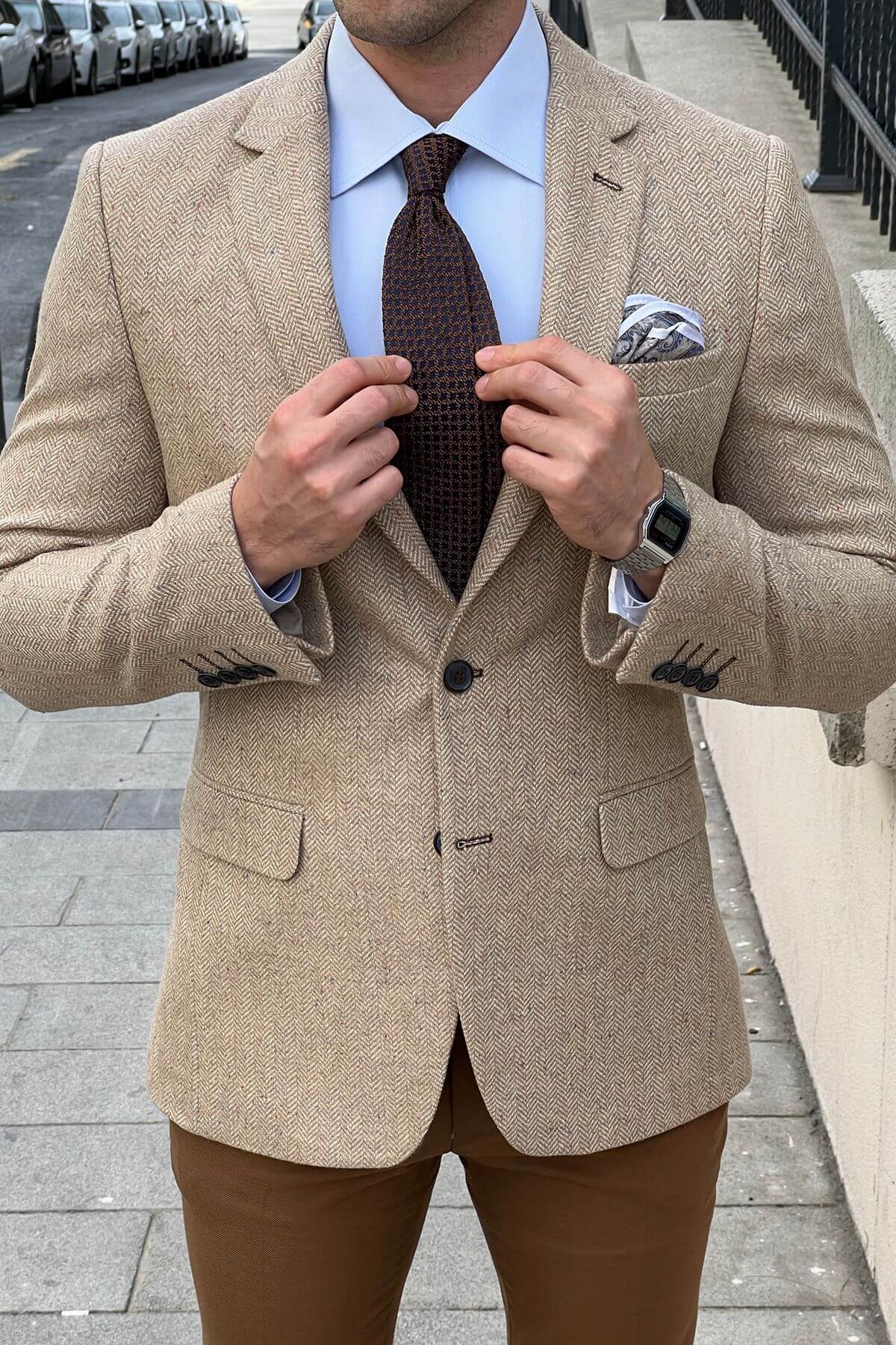 Man adjusting his beige blazer with a patterned tie and pocket square.