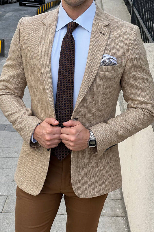Man wearing a beige blazer, brown pants, and a patterned tie on a city street.