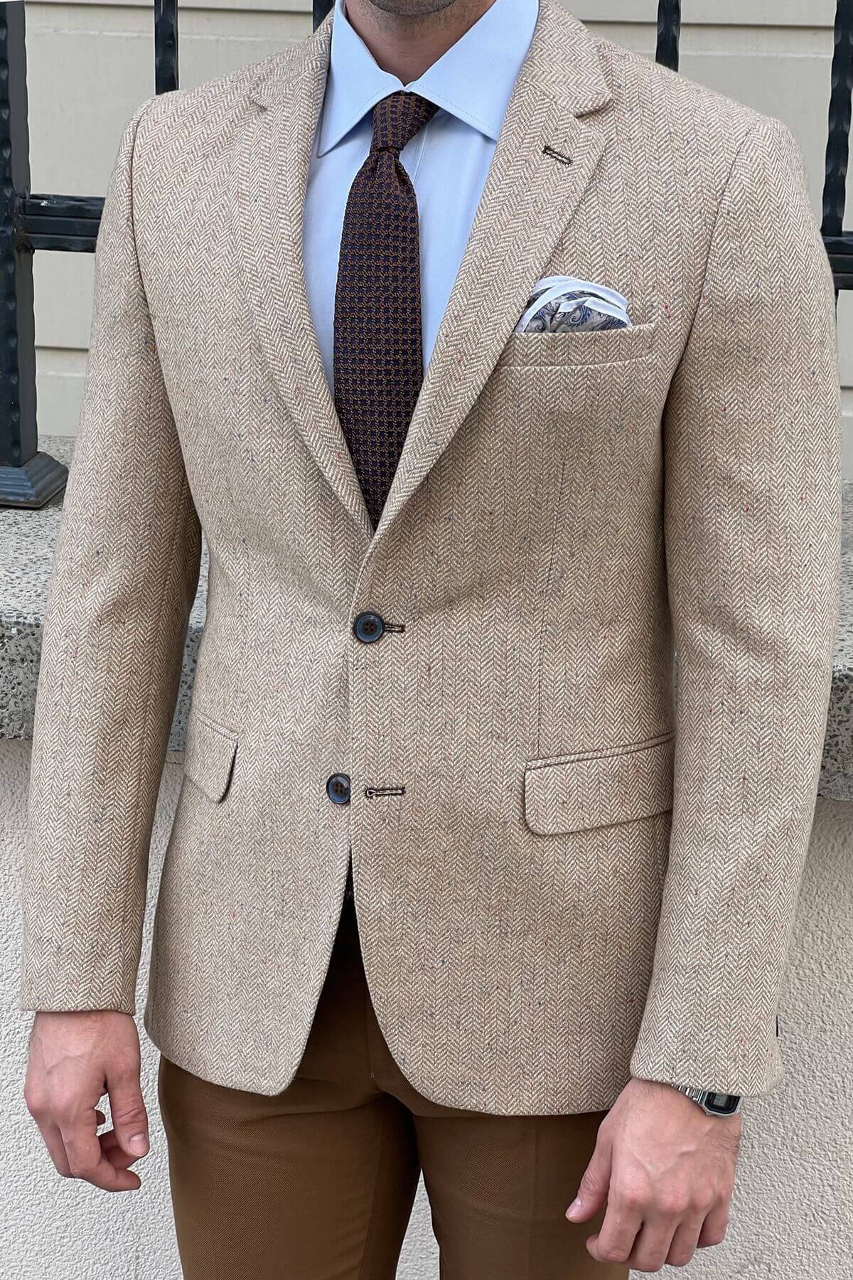 Man wearing a beige blazer, brown pants, and patterned tie outdoors.