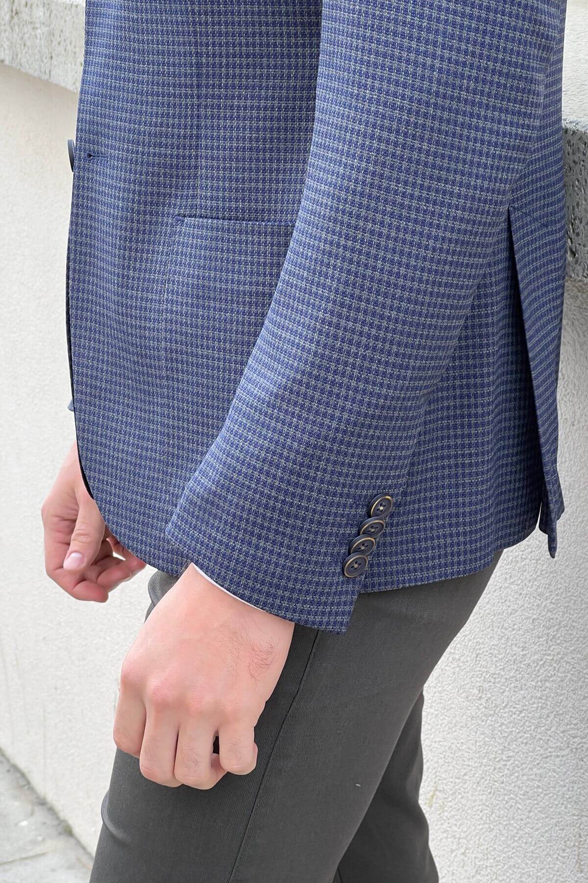 Close-up of a person wearing a blue checkered jacket with gray pants against a light gray background