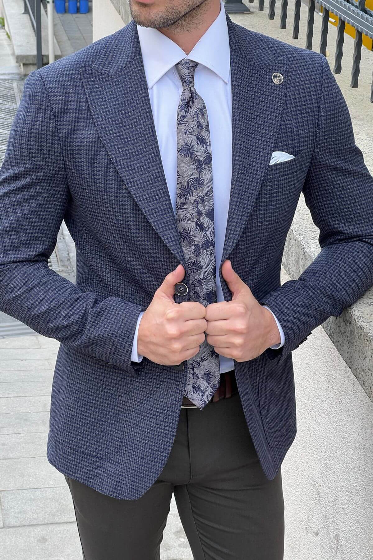 Man wearing a blue checkered suit with a patterned tie outdoors.