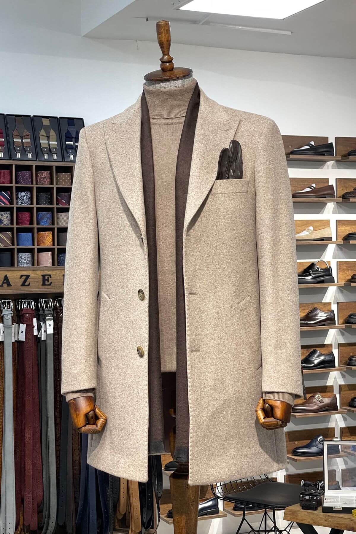 Beige overcoat on a mannequin in a store setting with shelves and racks in the background.