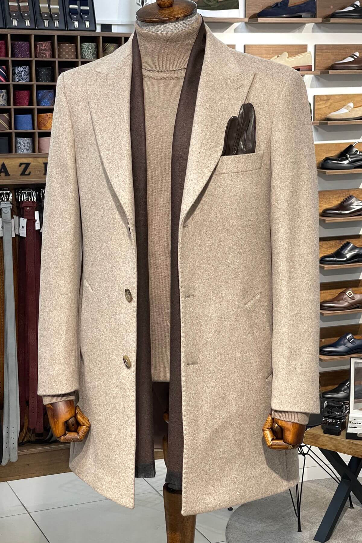 Beige overcoat on a mannequin with a brown tie and pocket square in a store setting.