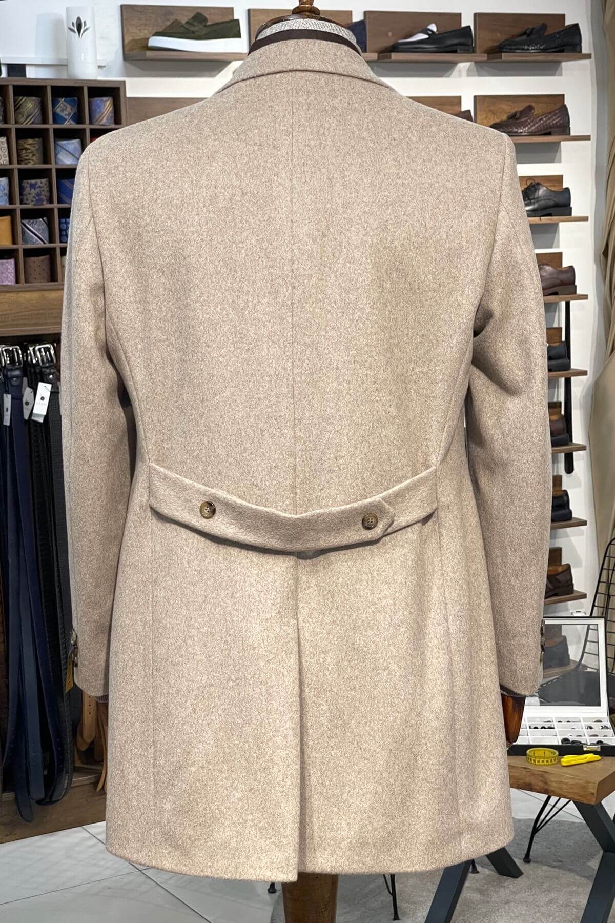 Beige coat on a mannequin in a store setting with shelves in the background