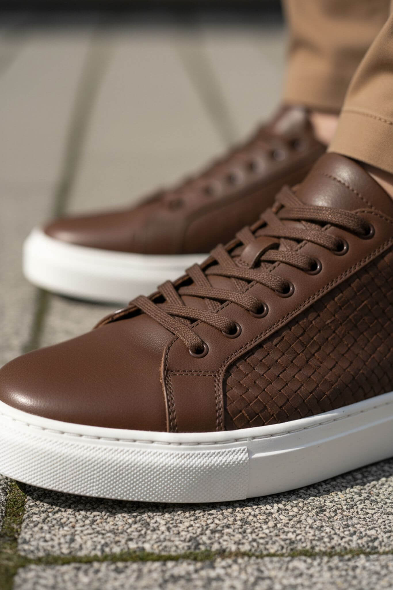 Brown leather sneakers with white soles on a textured surface