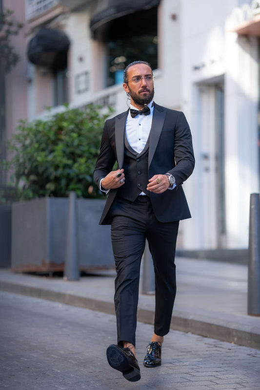 Elegant man wearing a black tuxedo with a bow tie, perfect for fall weddings and formal events, walking confidently in an urban setting.