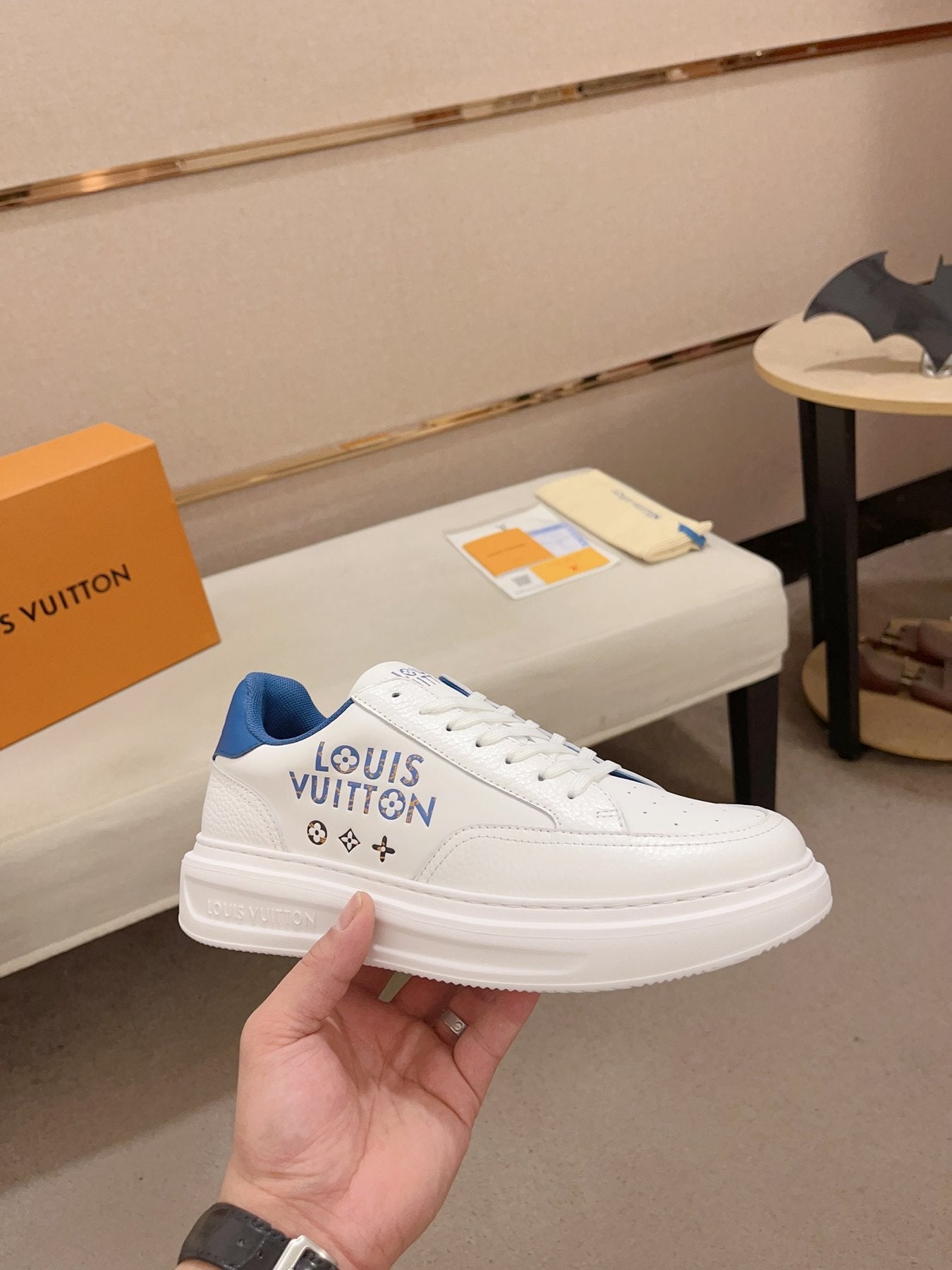 Louis Vuitton white and blue logo low-top sneakers angled side view held in hand