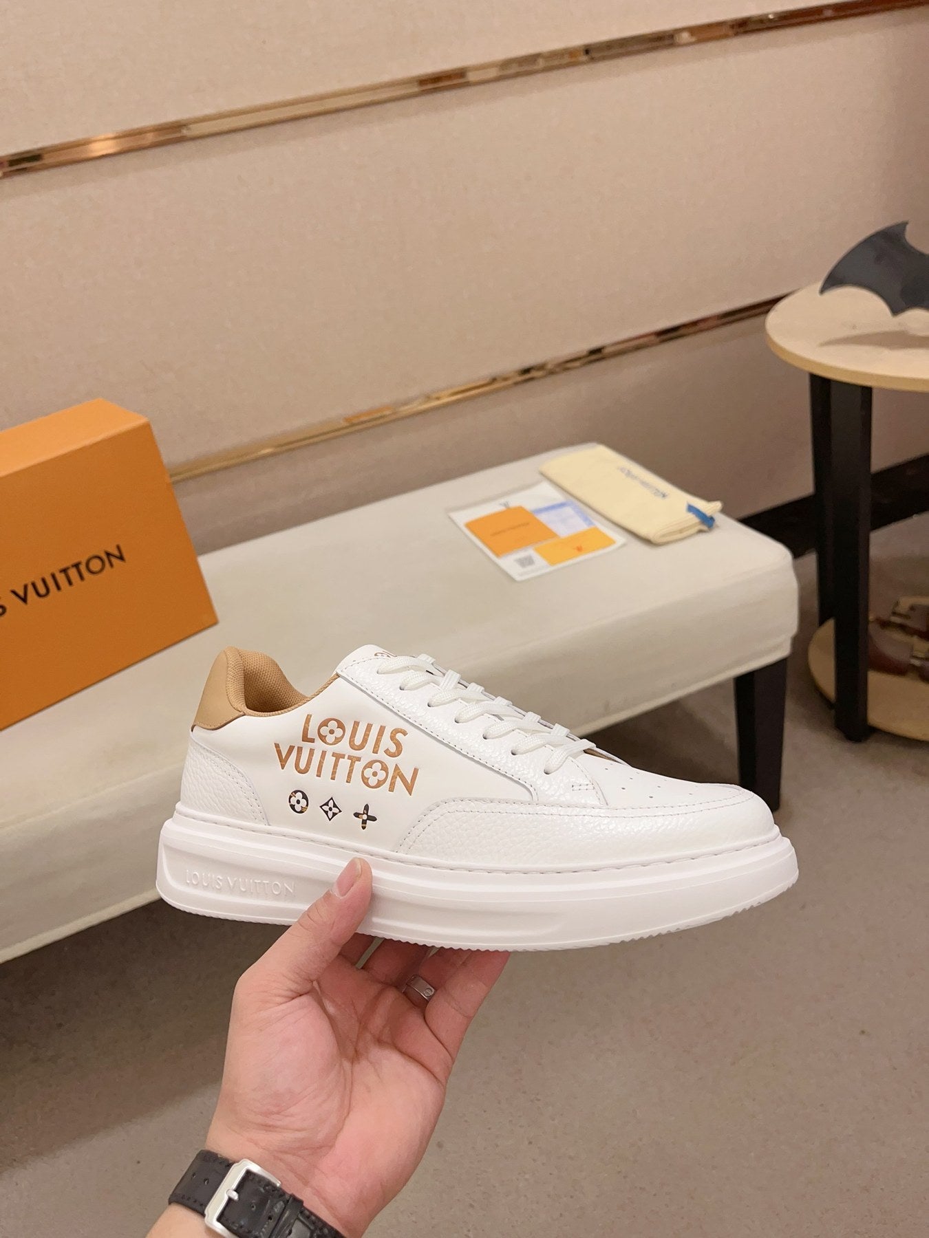Louis Vuitton white and tan logo low-top sneakers angled side view held in hand