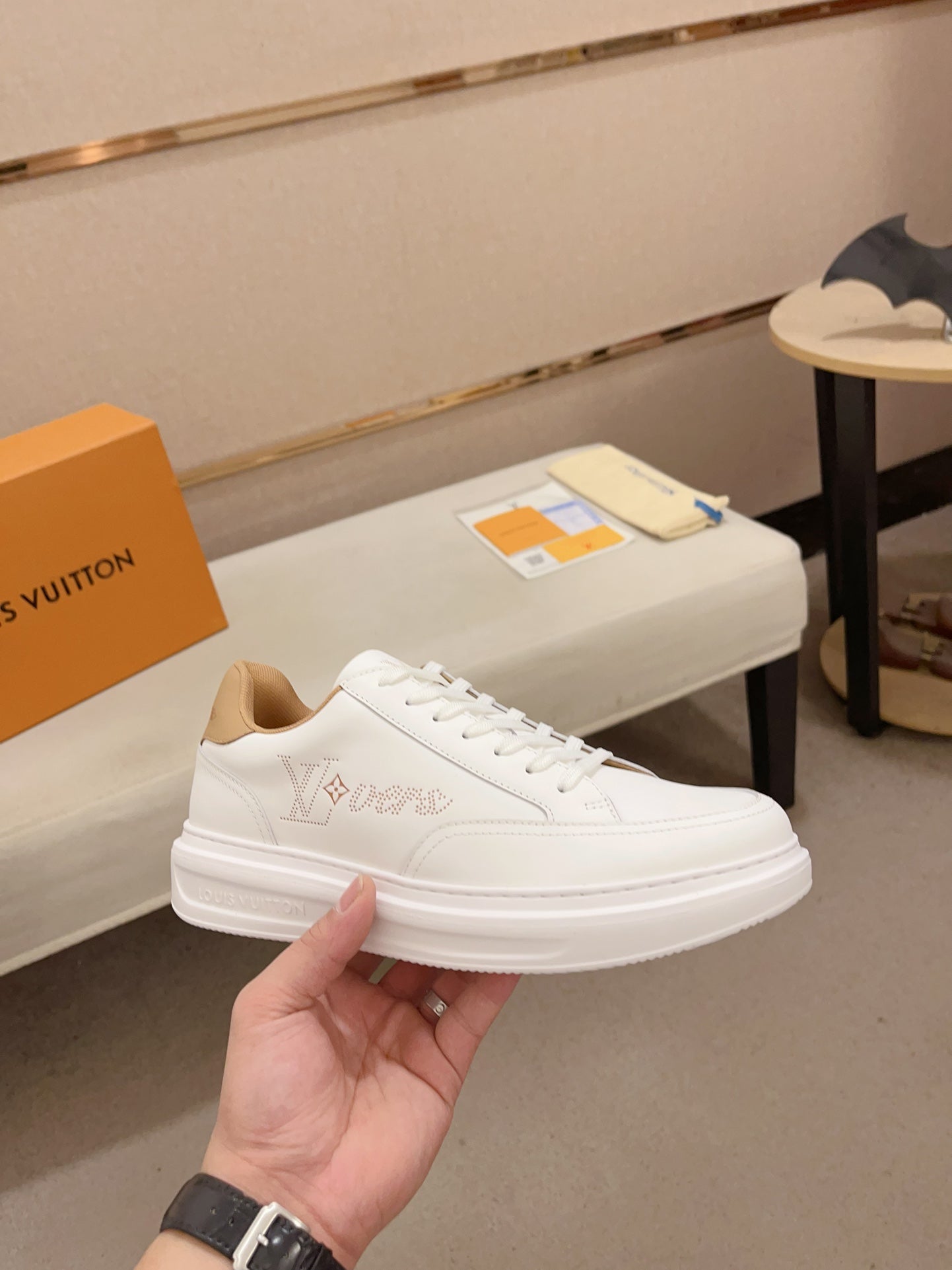 Louis Vuitton white and tan perforated LV low-top sneakers angled side view held in hand