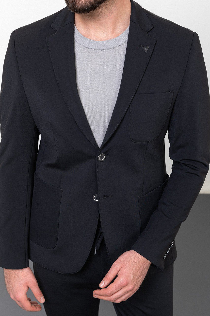 Man wearing a navy blue casual suit with a grey shirt and white sneakers.