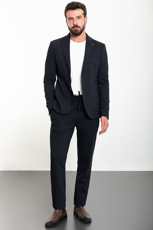 Man wearing a navy blue suit with a brown shirt and white sneakers.