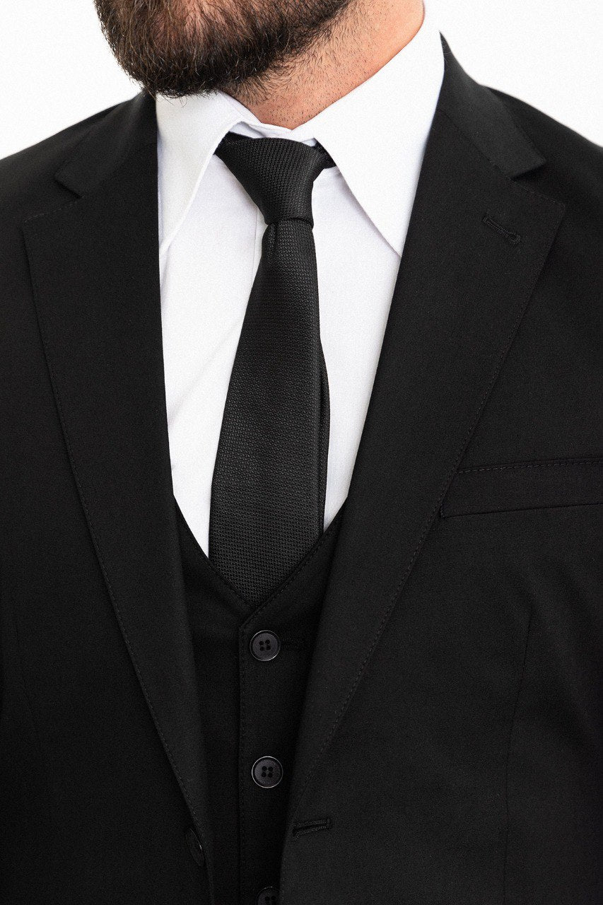 Man wearing a black 3-piece suit with a white shirt and black tie.