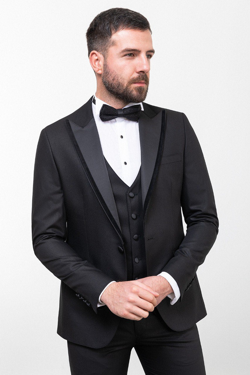 Man wearing an Onyx Elegance Tuxedo with a satin peak lapel, flap pockets, and a slim fit, perfect for black-tie events and weddings.