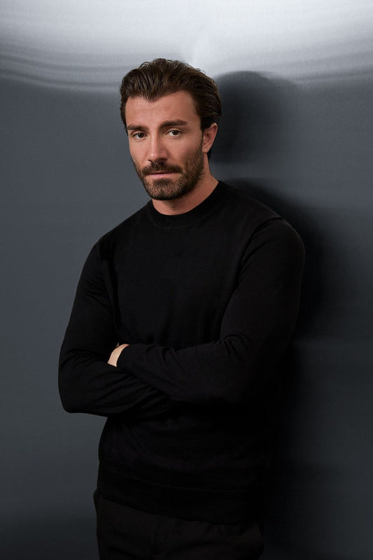Man wearing a black crew neck sweater with his arms folded