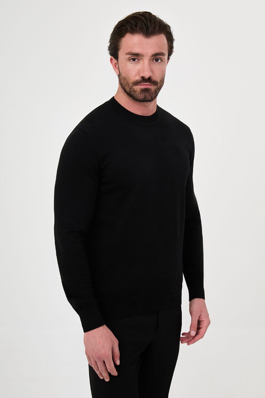 Angled view of a man wearing a black crew neck sweater