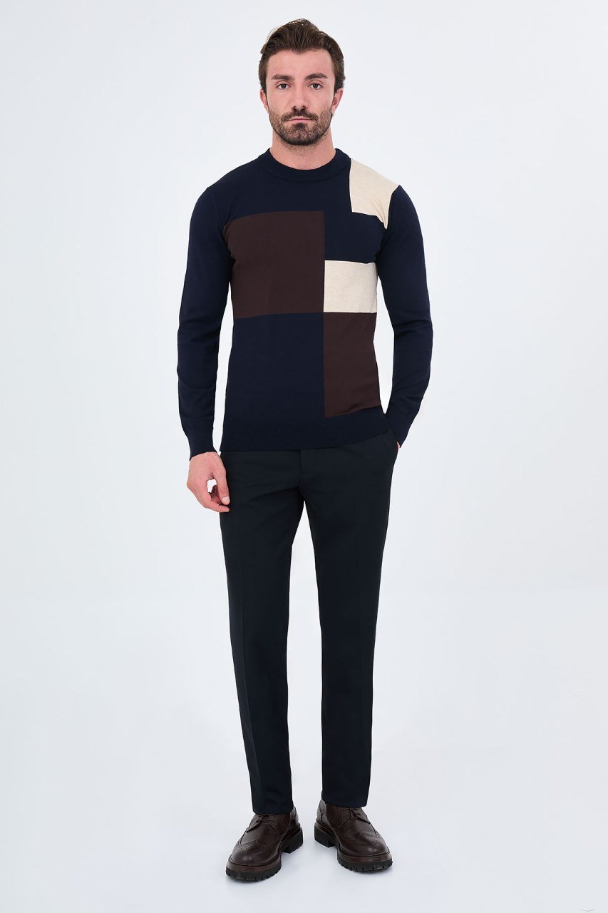 Man wearing a navy blue asymmetric colour-block sweater with black trousers