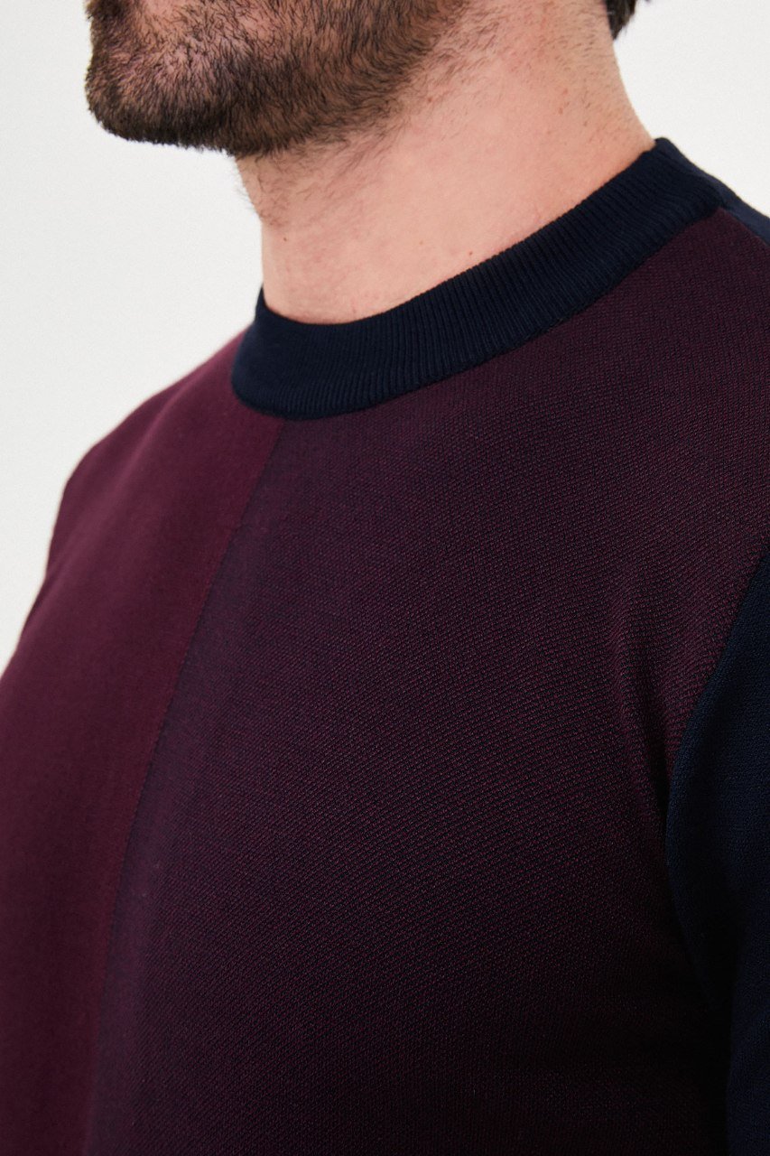 Close-up of the navy blue and burgundy colour-block sweater's crew neckline and contrasting knit panels