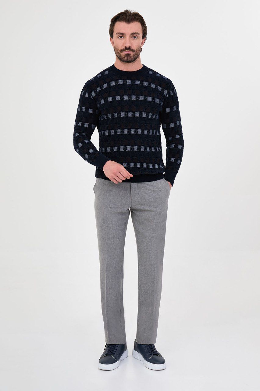 Man wearing a navy blue geometric crew neck sweater with grey trousers